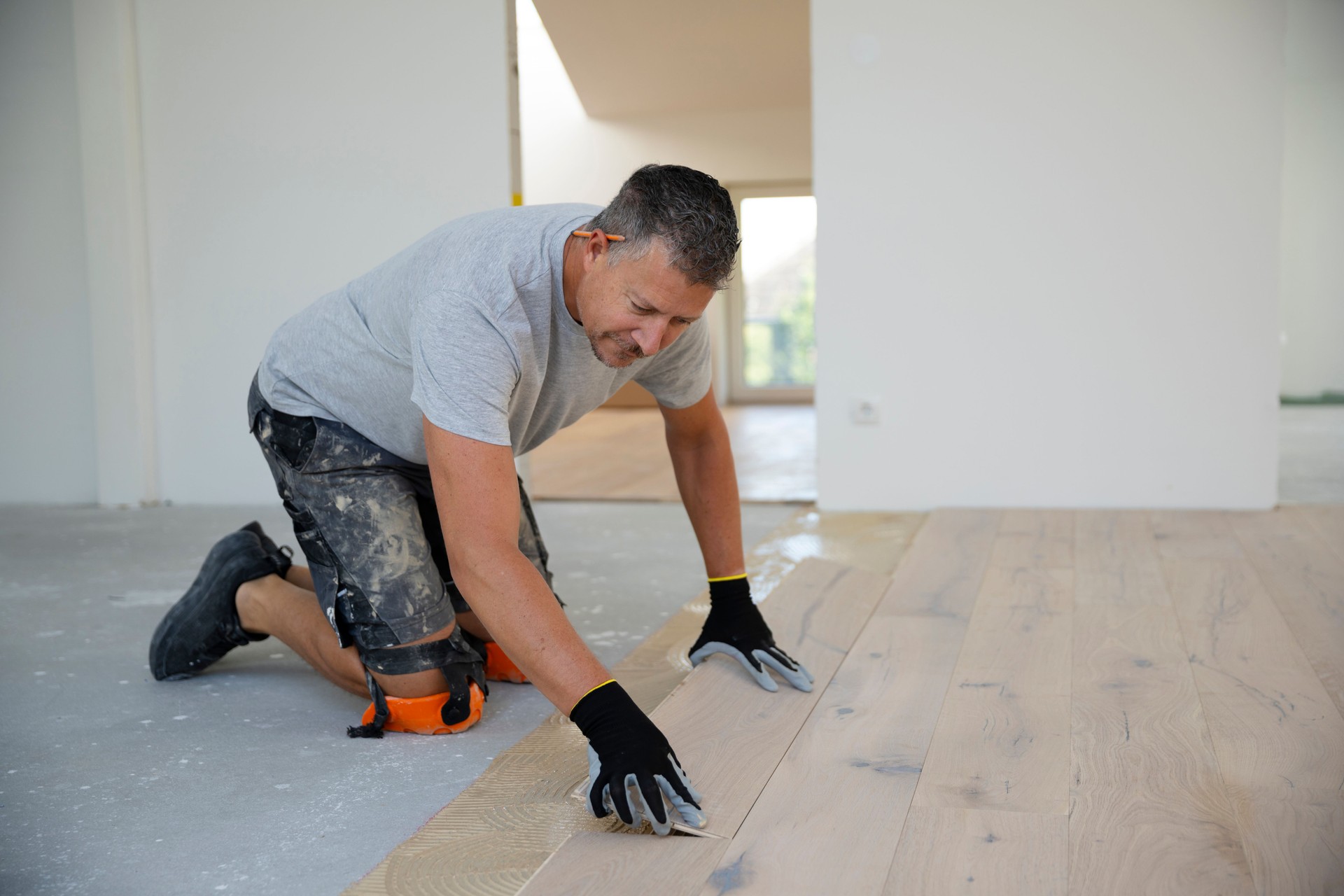 middle-aged man with gray hair glues, lays parquet floor